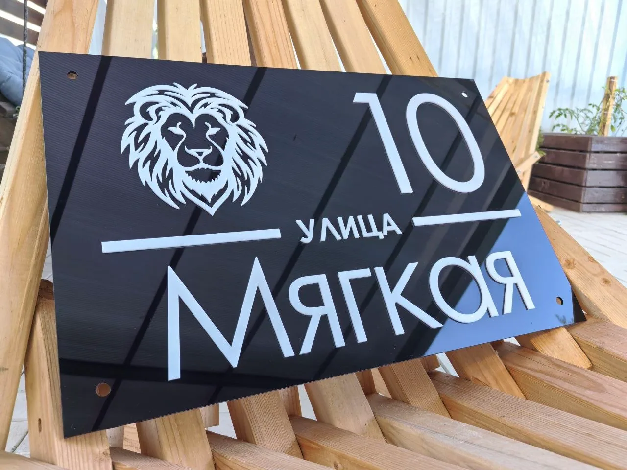 Черная глянцевая табличка из акрила с белым номером 10, названием улицы Мягкая и графическим логотипом головы льва