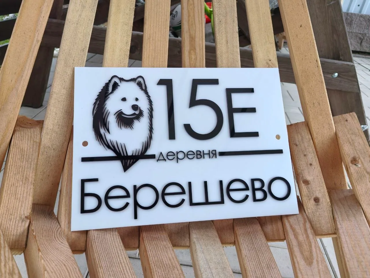 Белая акриловая табличка с объемным номером 15Е, названием деревни Берешево и черным силуэтом собаки породы самоед (шпиц)