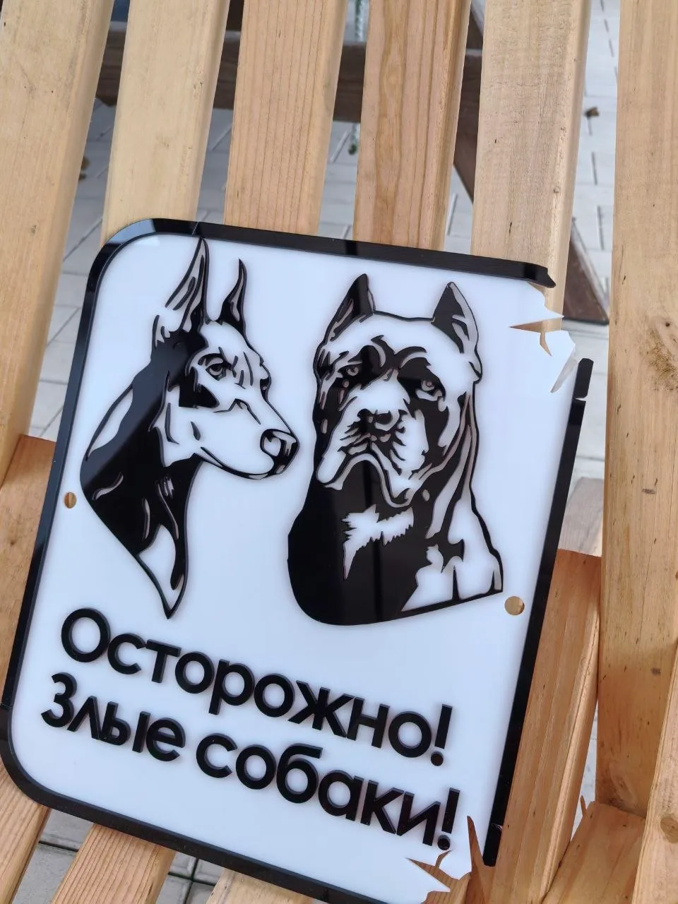 Белая адресная табличка с объемными черными изображениями голов добермана и кане-корсо и предупреждающей надписью «Осторожно! Злые собаки!»